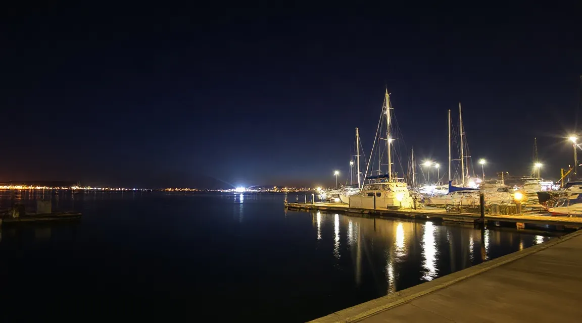 Marina at night with moored sailboats and harbor lights reflected on the water