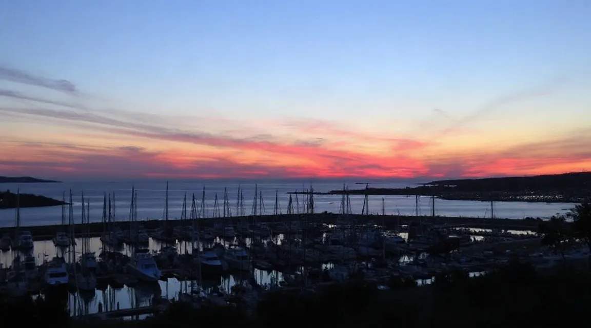Pink and orange sky over a darkened harbor at dusk